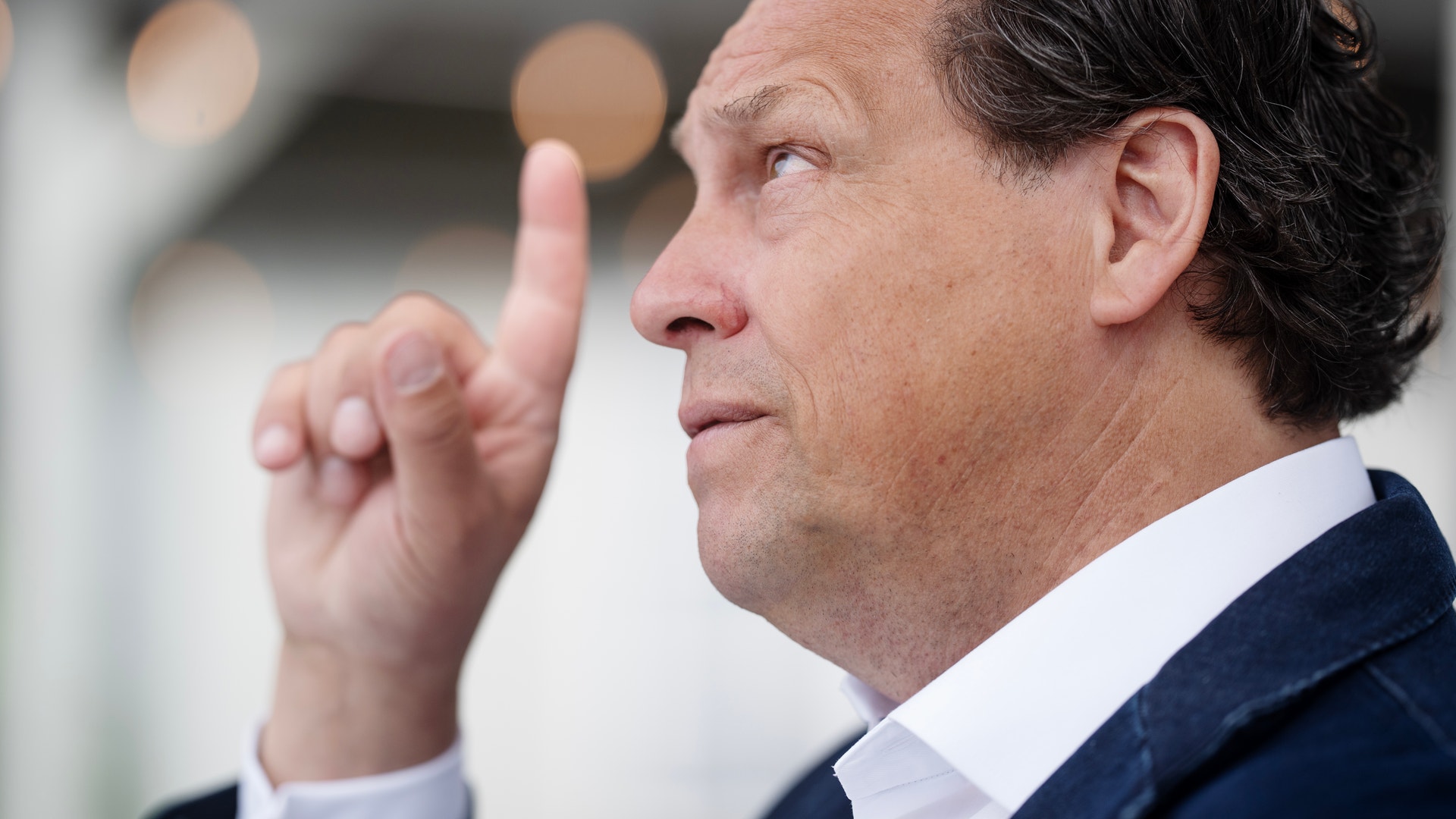 Porträttfoto av en man i kostym som pekar uppåt med sitt finger.