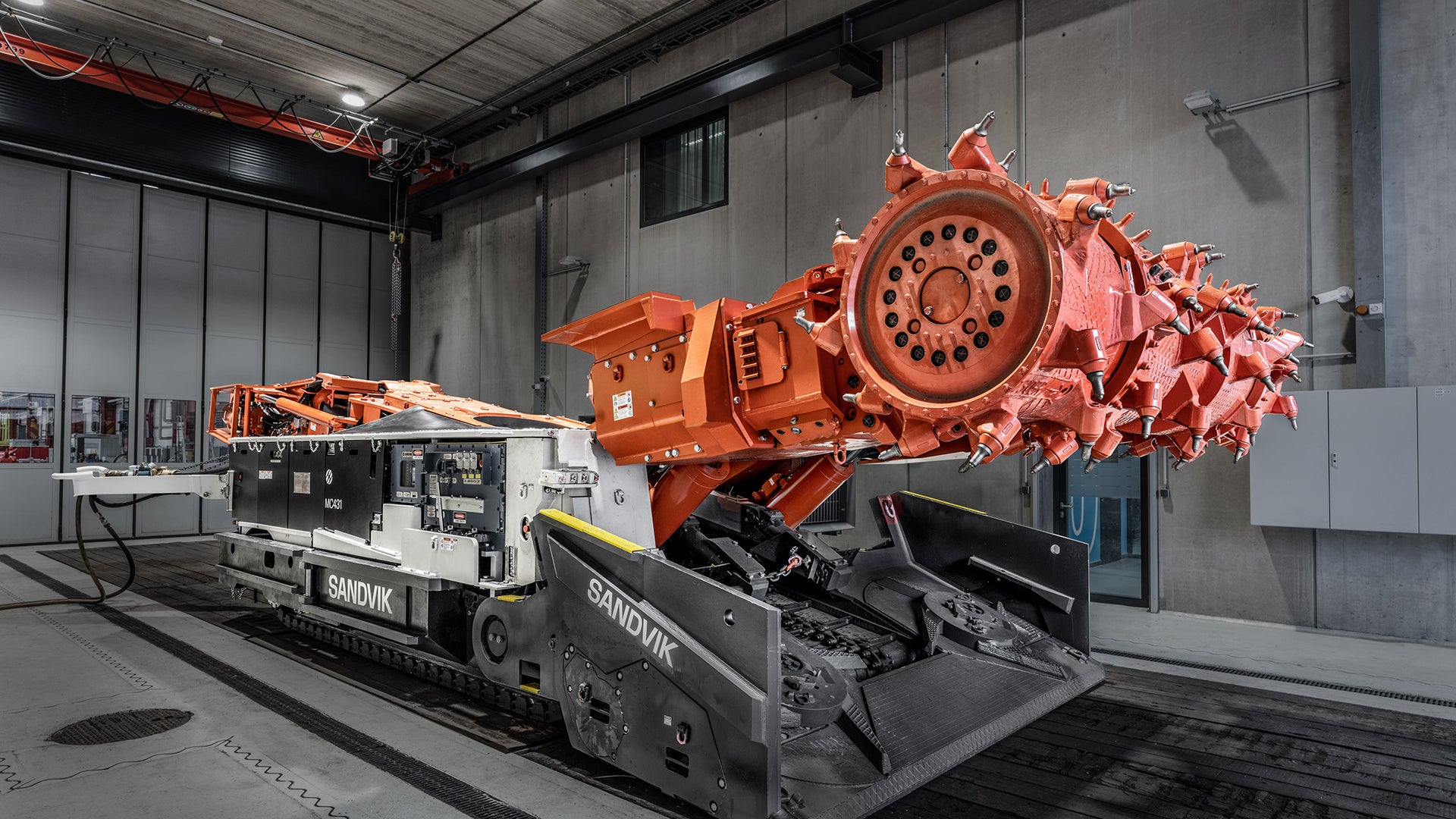 En stor orange industriell krosmaskin monterad på en svart transportvagn i en fabrikshall.