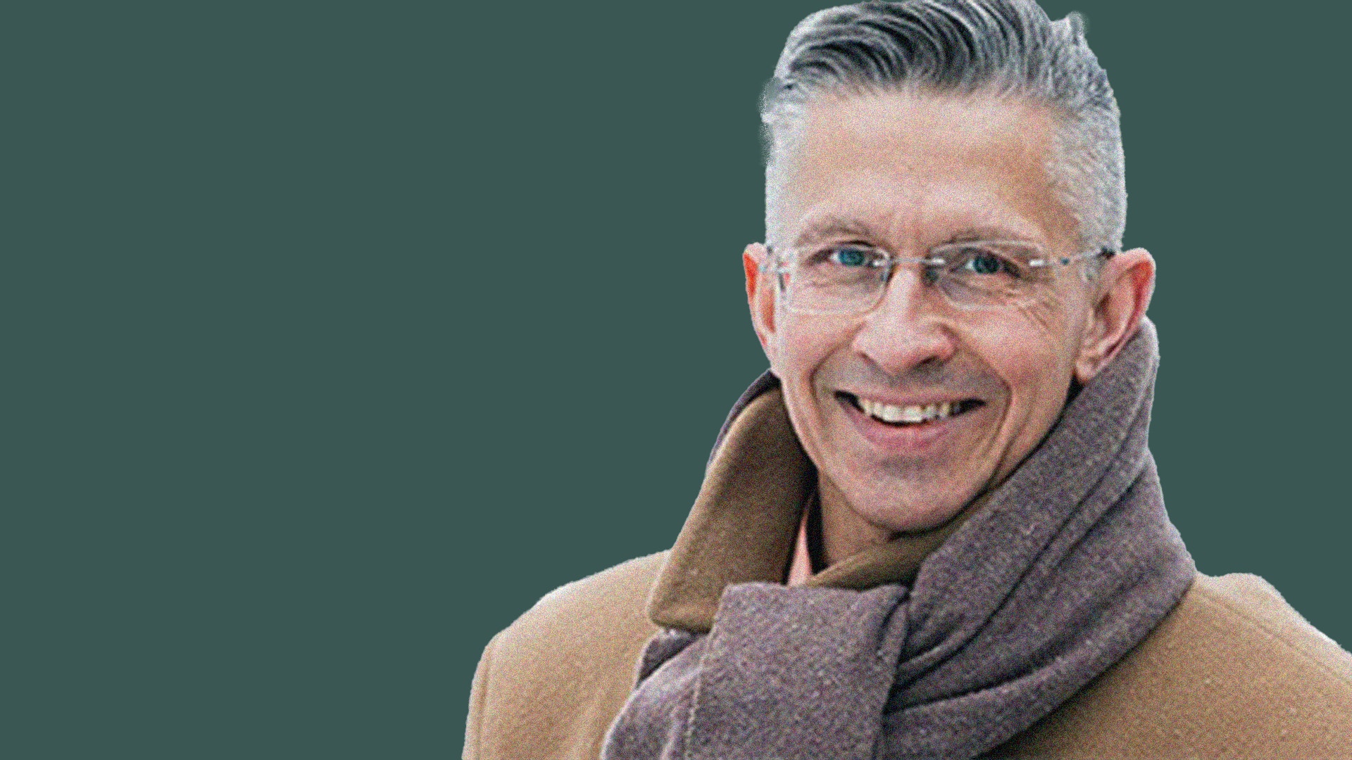 Porträttfoto av en man med glasögon som ler mot kameran. Han bär en beige tröja och grå halsduk mot en grön bakgrund.