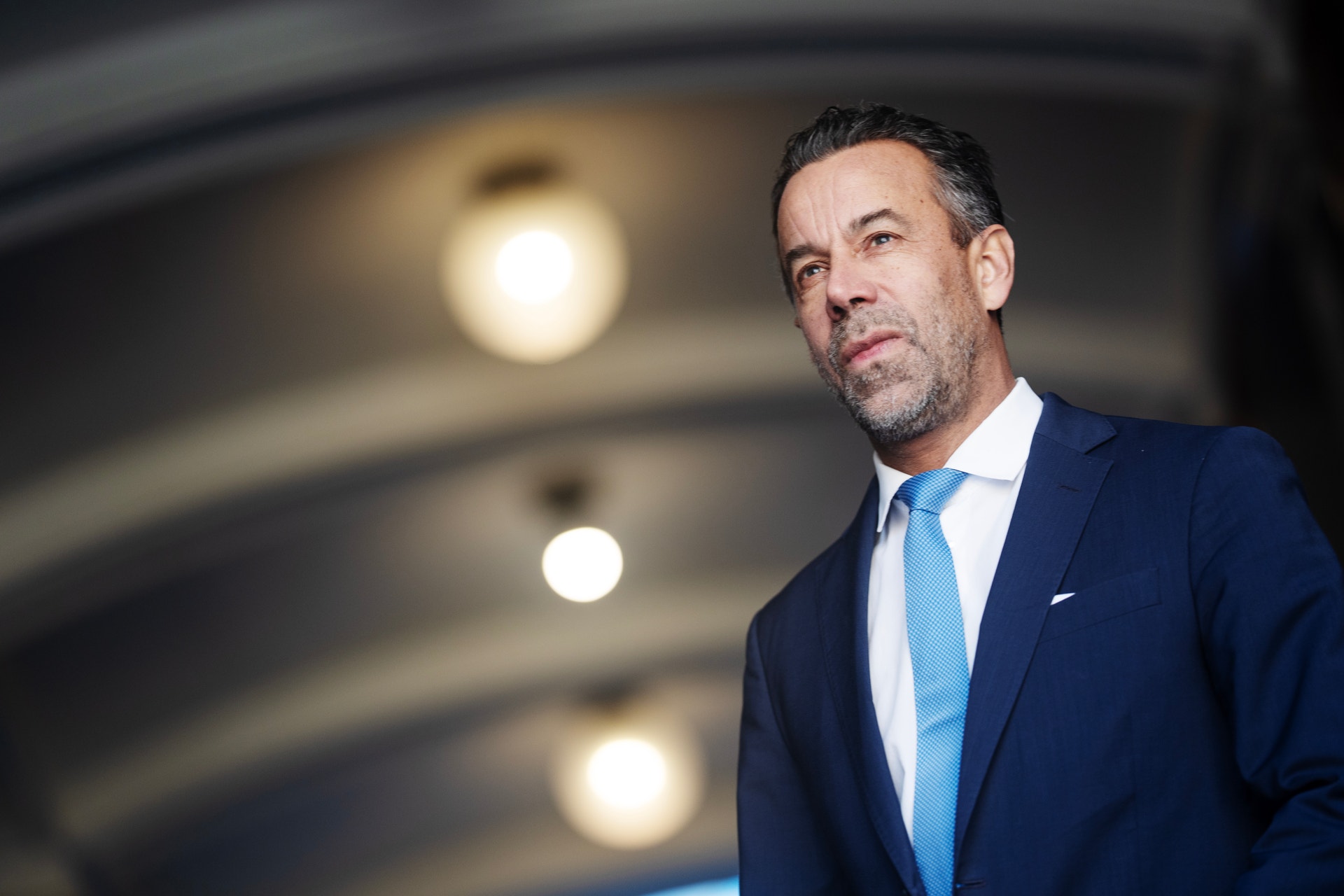 Christian Kopfer, en man i mörk kostym och ljusblå slips, tittar allvarligt åt sidan.