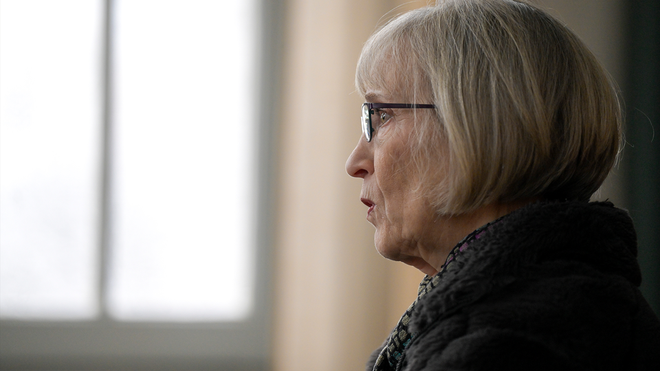 Profilbild av Claudia Goldin med grått hår och glasögon, klädd i en svart jacka. Hon är fotograferad från sidan mot en suddig bakgrund med fönster.