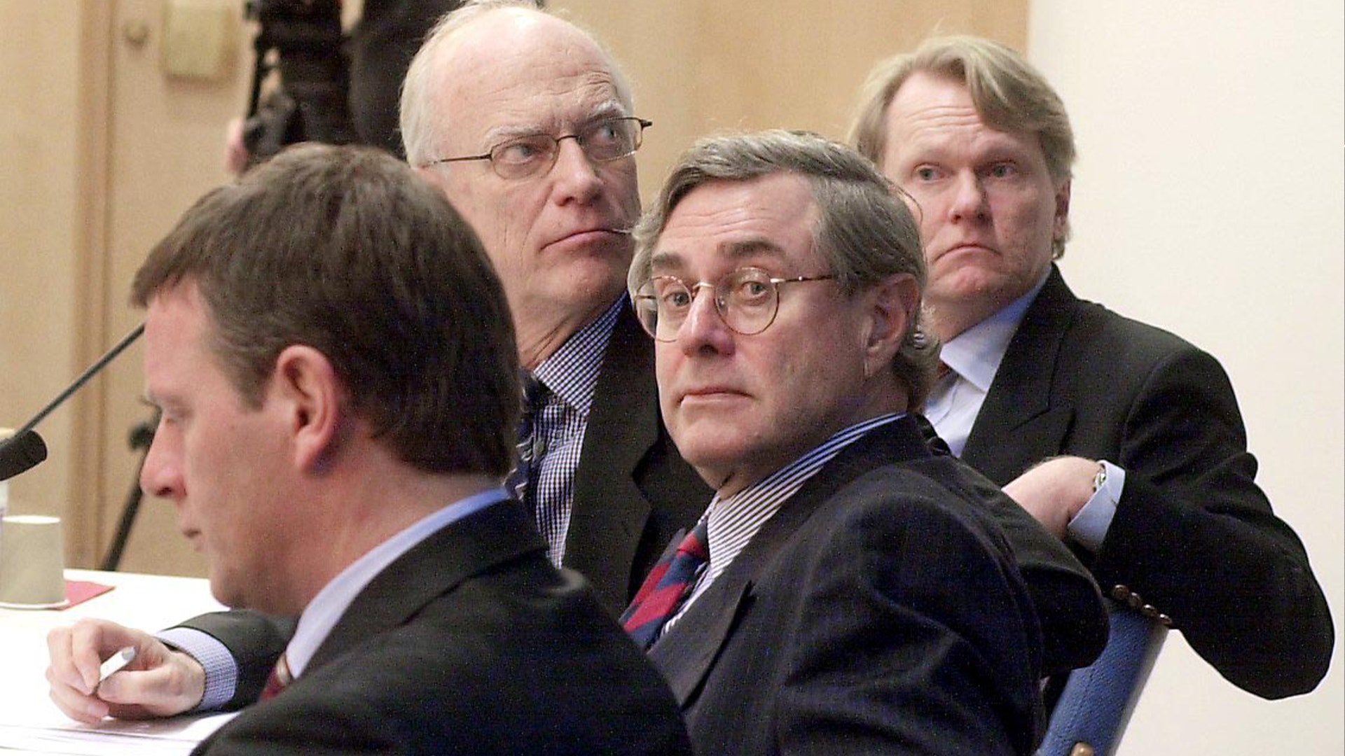 Fyra män i kostym sitter tillsammans i ett formellt möte.