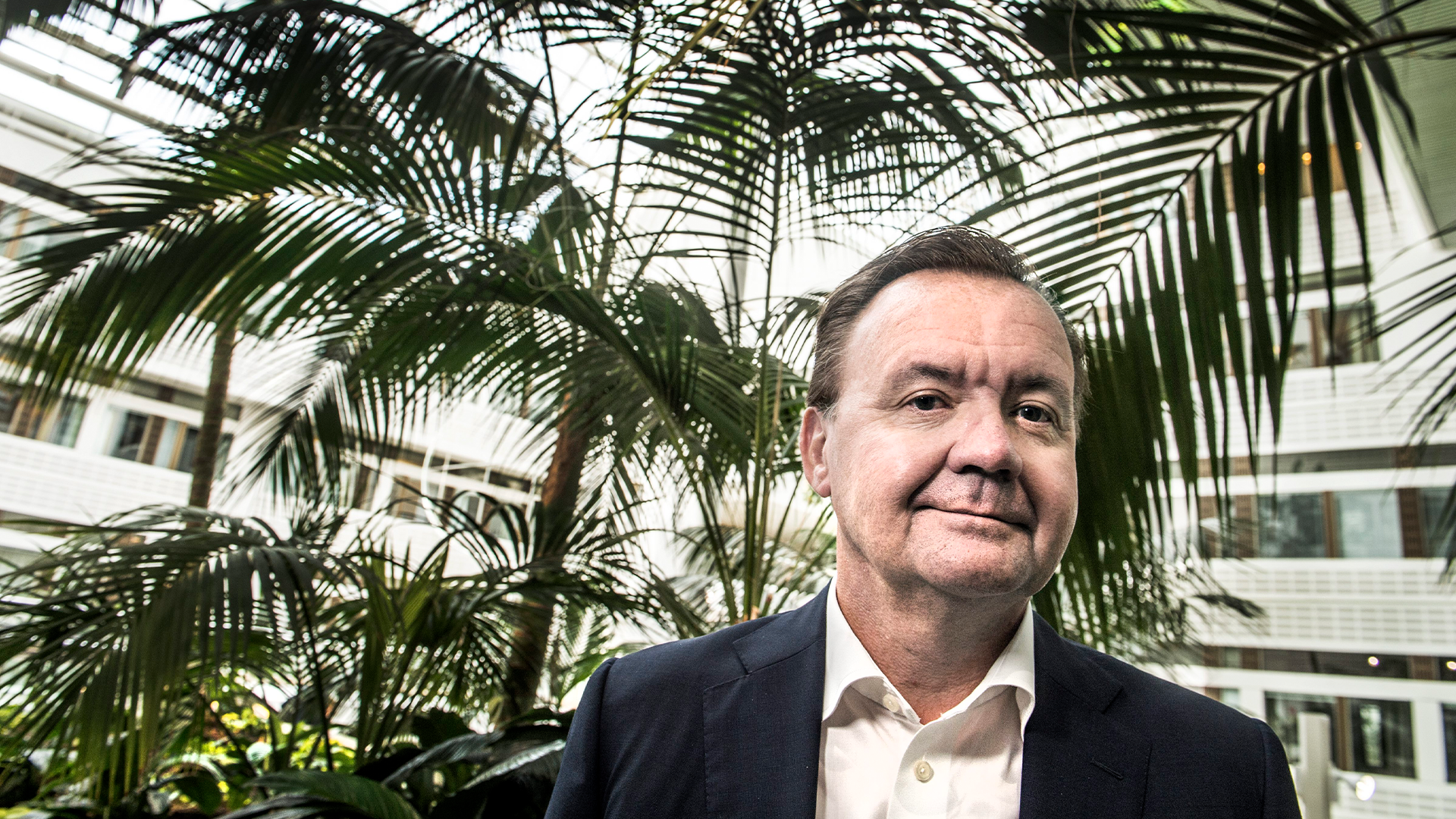 Porträtt av Karl-Henrik Sundström, man i mörk kavaj och ljus skjorta framför gröna växter