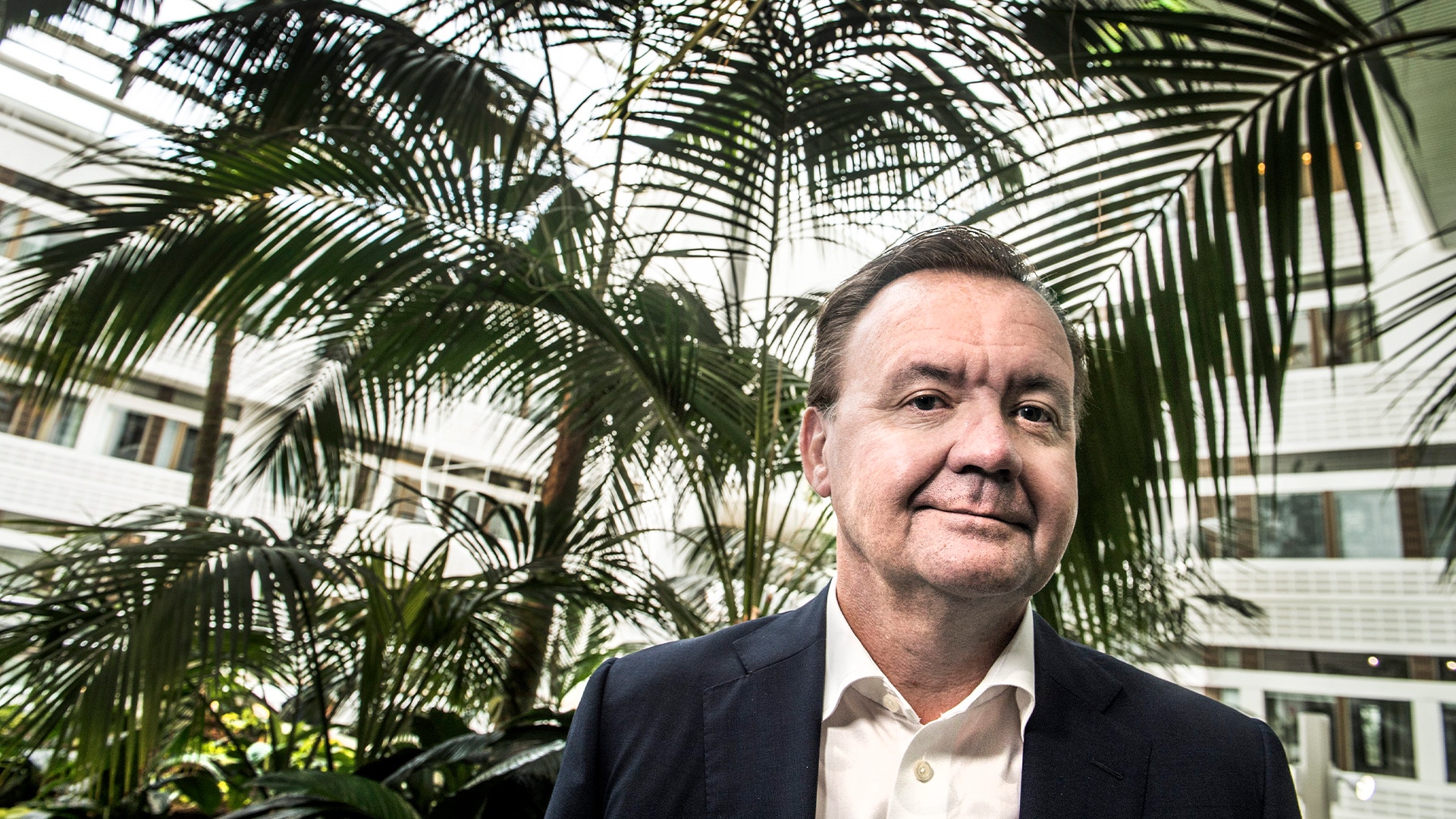 Porträtt av Karl-Henrik Sundström, man i mörk kavaj och ljus skjorta framför gröna växter