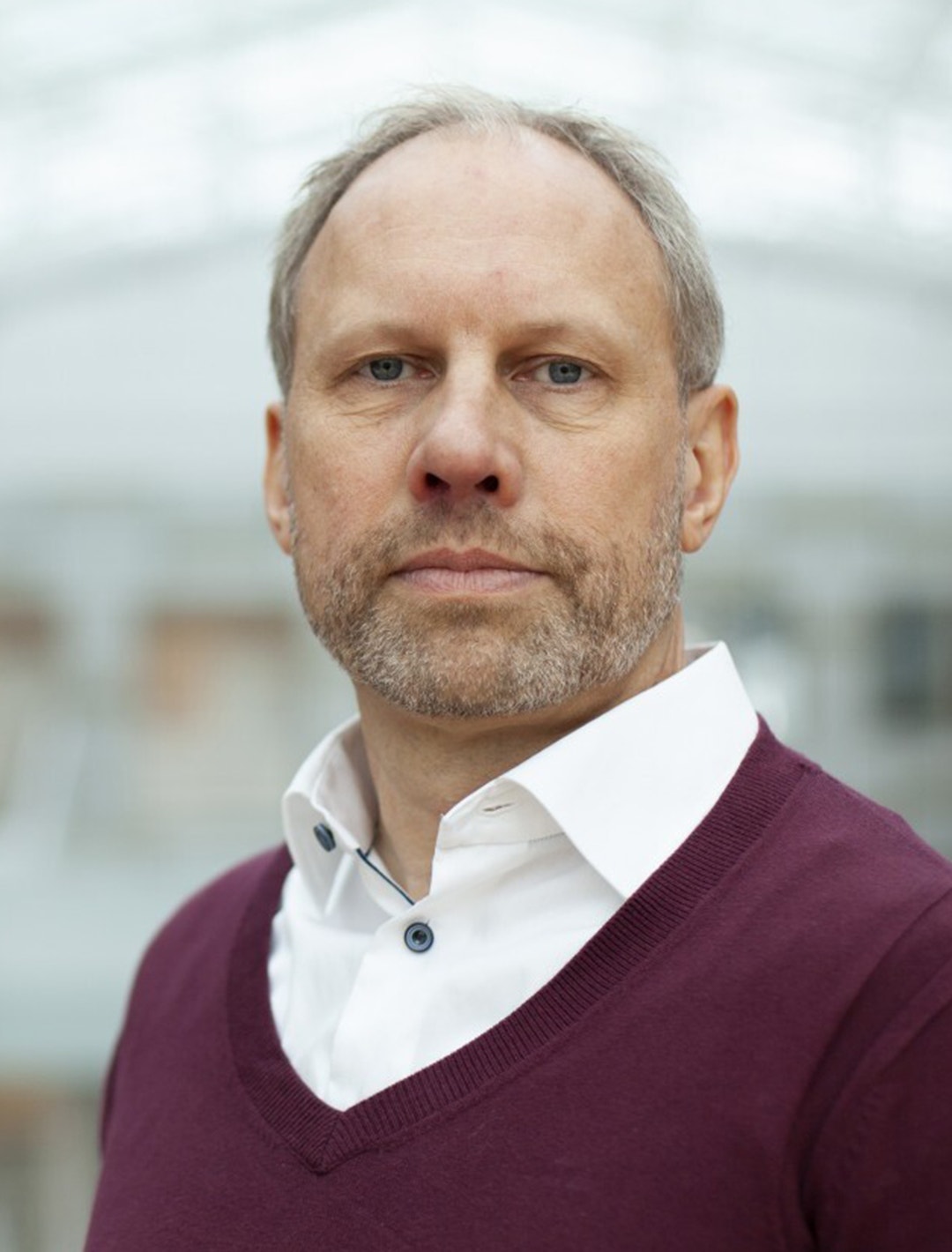 Porträttbild på David Melin i vit skjorta och vinröd pullover.