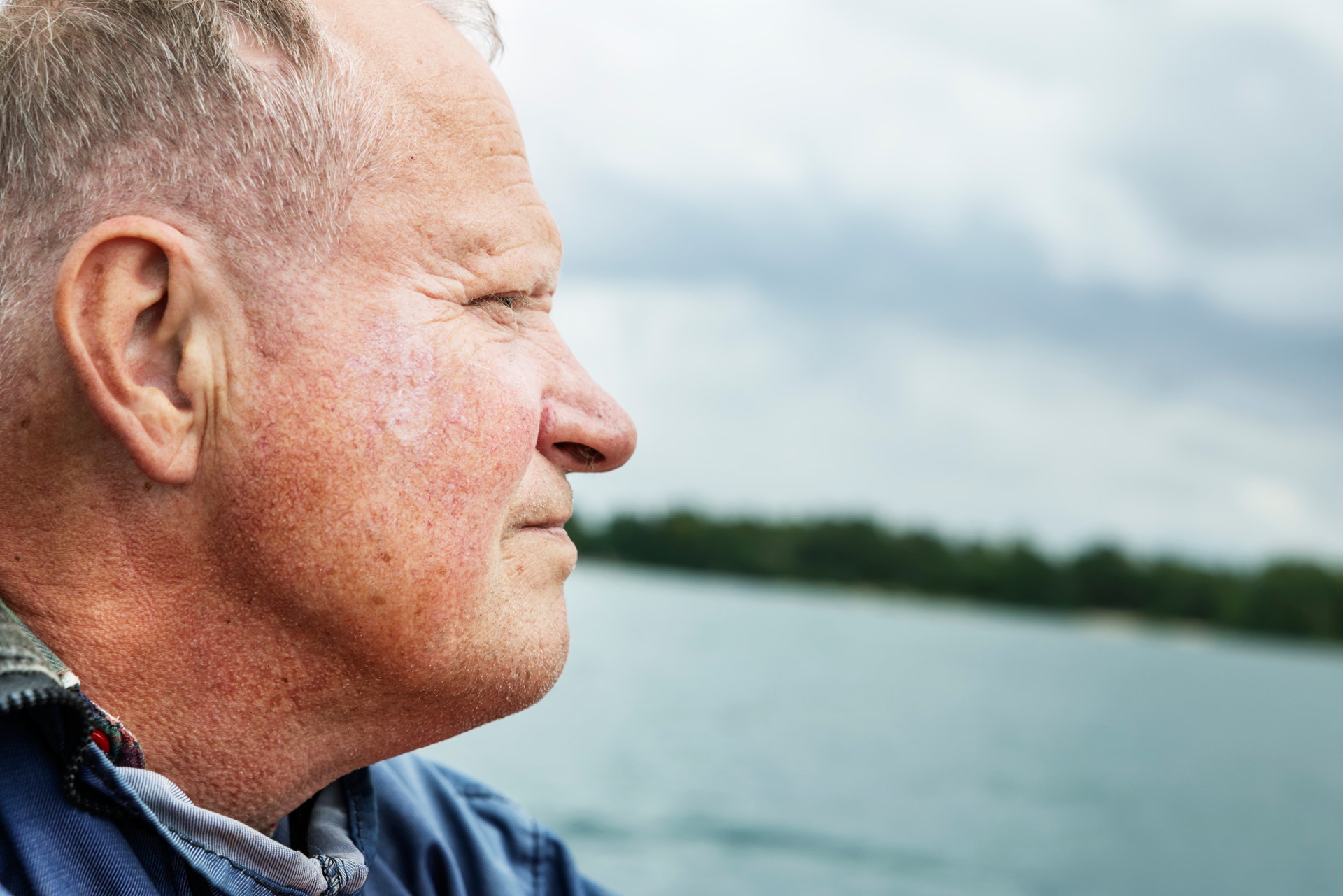 Profilbild av en man som tittar ut över vatten med träd och himmel i bakgrunden.
