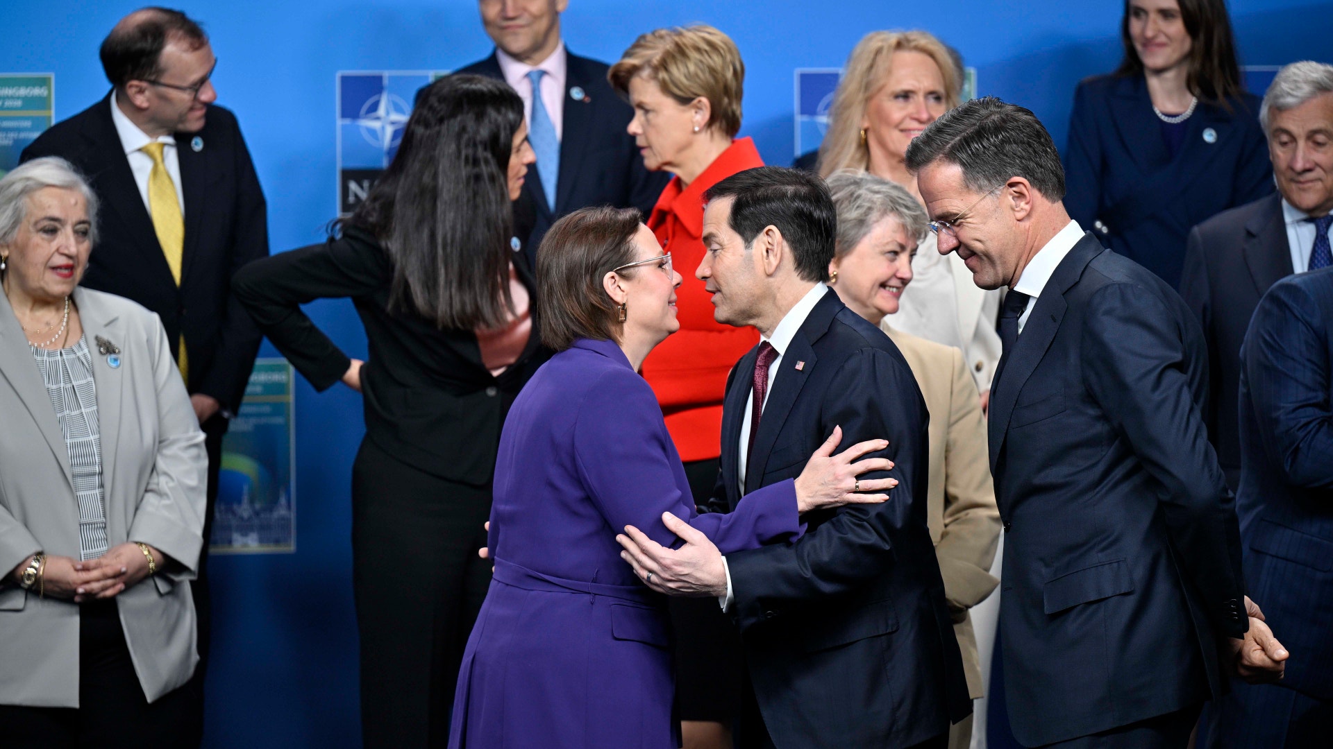 Gruppfoto från ett officiellt politiskt möte med flera politiker i formell klädsel som står tillsammans mot en blå bakgrund.