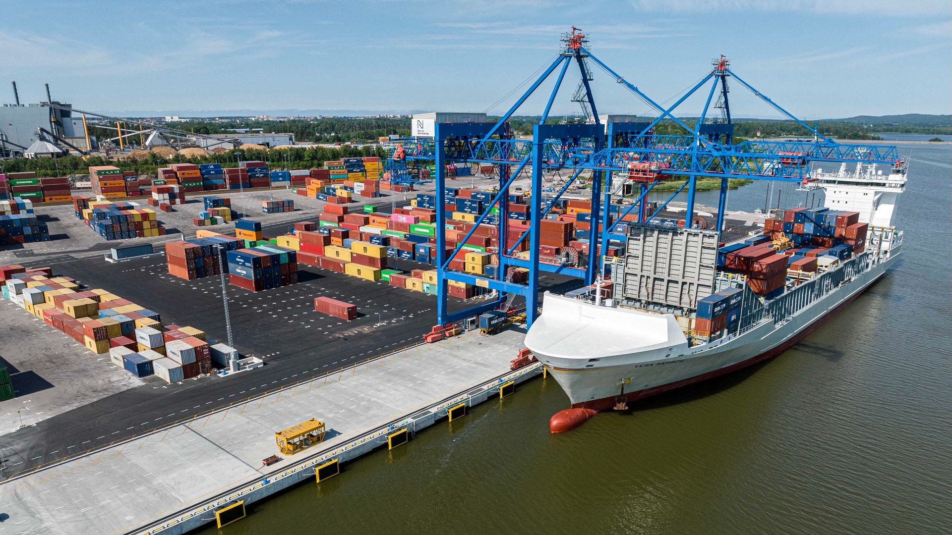 Fraktfartyg lastat med färgglada containerboxar vid en containerhamn med stora kranar för lastning och lossning.