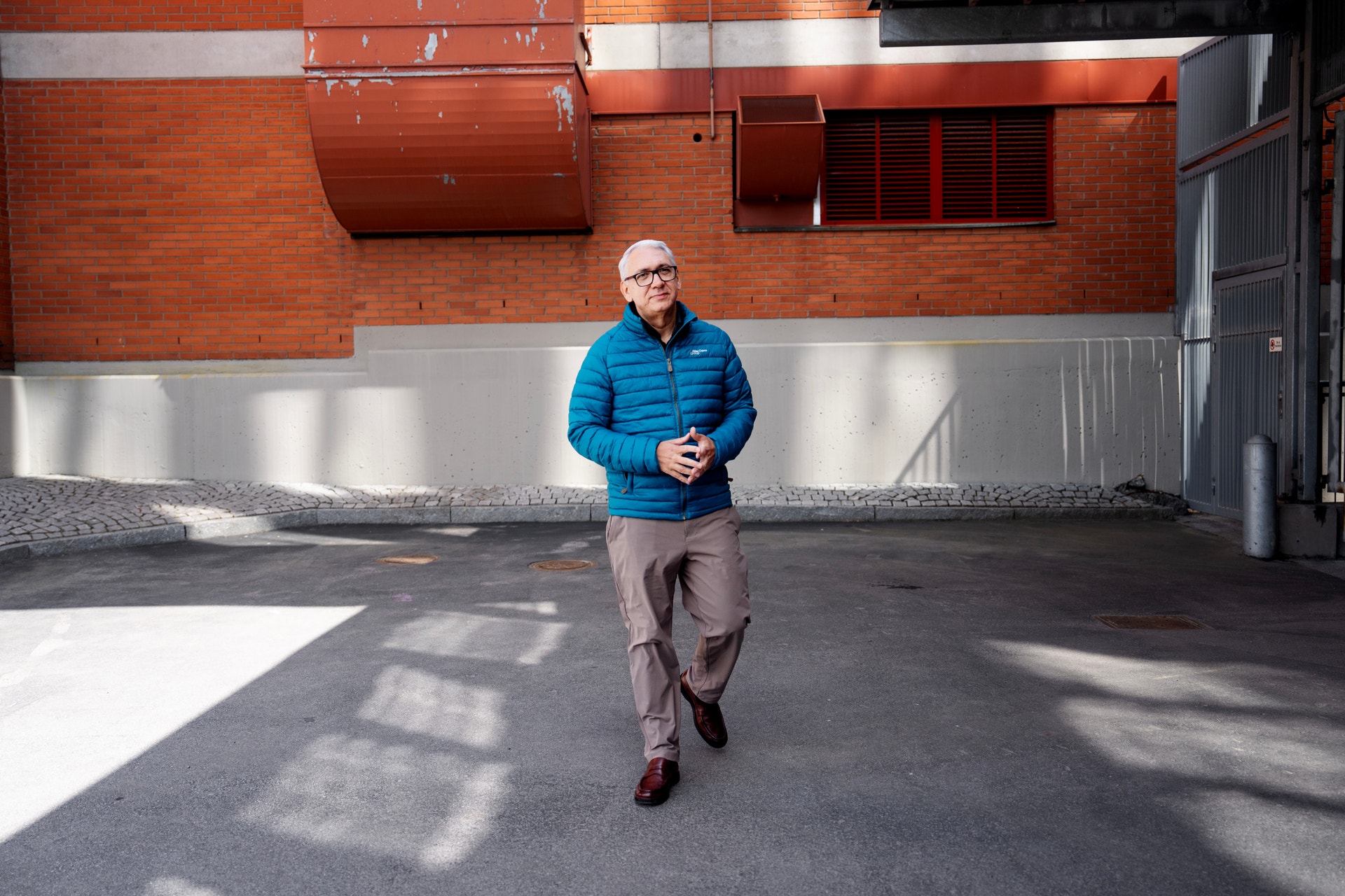 Man i blå jacka joggar framför en röd och vit byggnad.