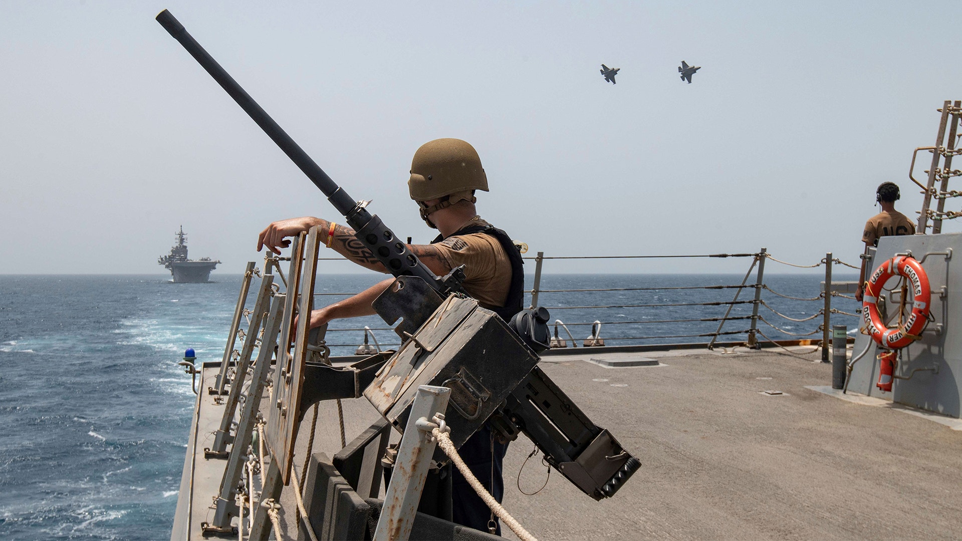 Militär personal på ett krigsfartyg opererar ett vapen medan de övervakar havet.