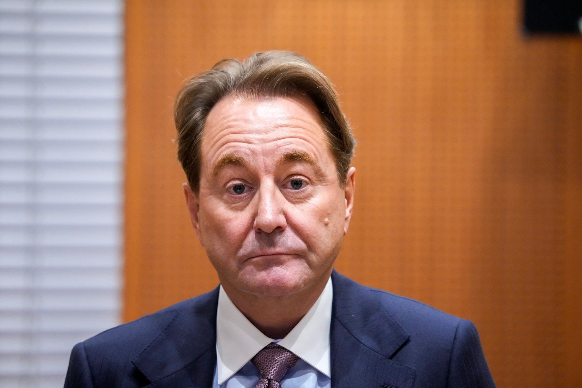 Kjell Inge Røkke, en man i mörkblå kostym och slips, tittar rakt in i kameran med allvarlig min.