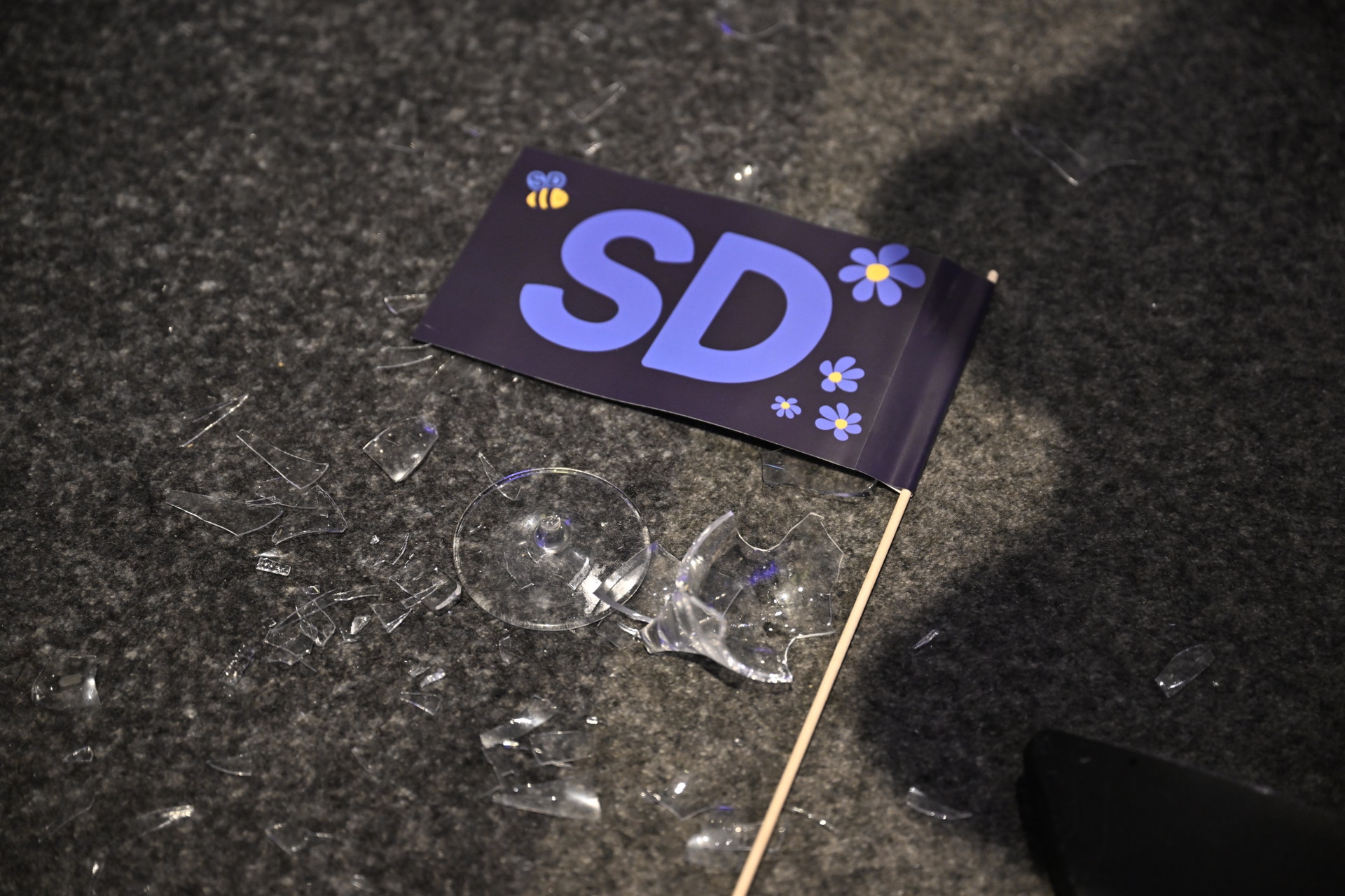 En liten flagga med texten SD ligger på en matta bland krossat glas.