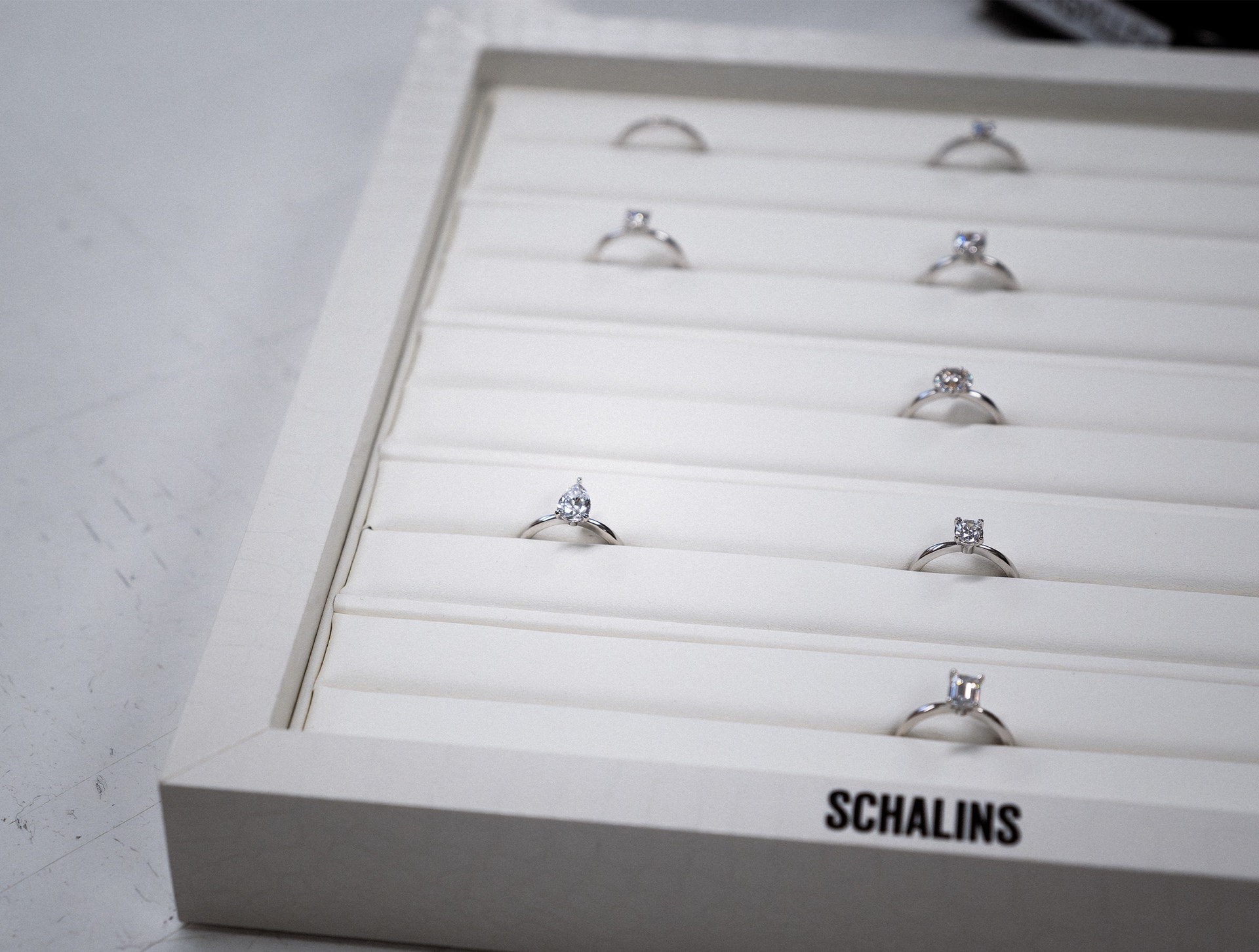 En vit smyckeslåda från Schalins med flera diamantringar utställda på vita kuddar.