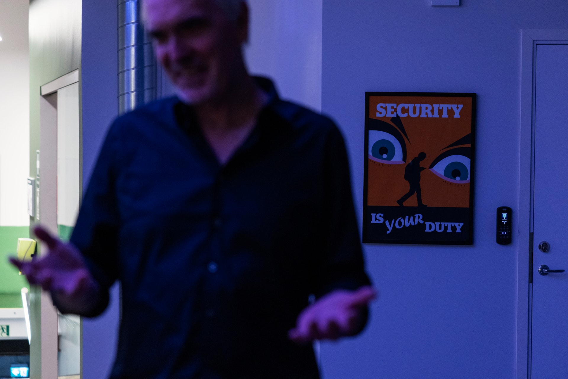 En person står framför en vägg med blå belysning. På väggen hänger en säkerhetsposter med texten "Security is your duty".