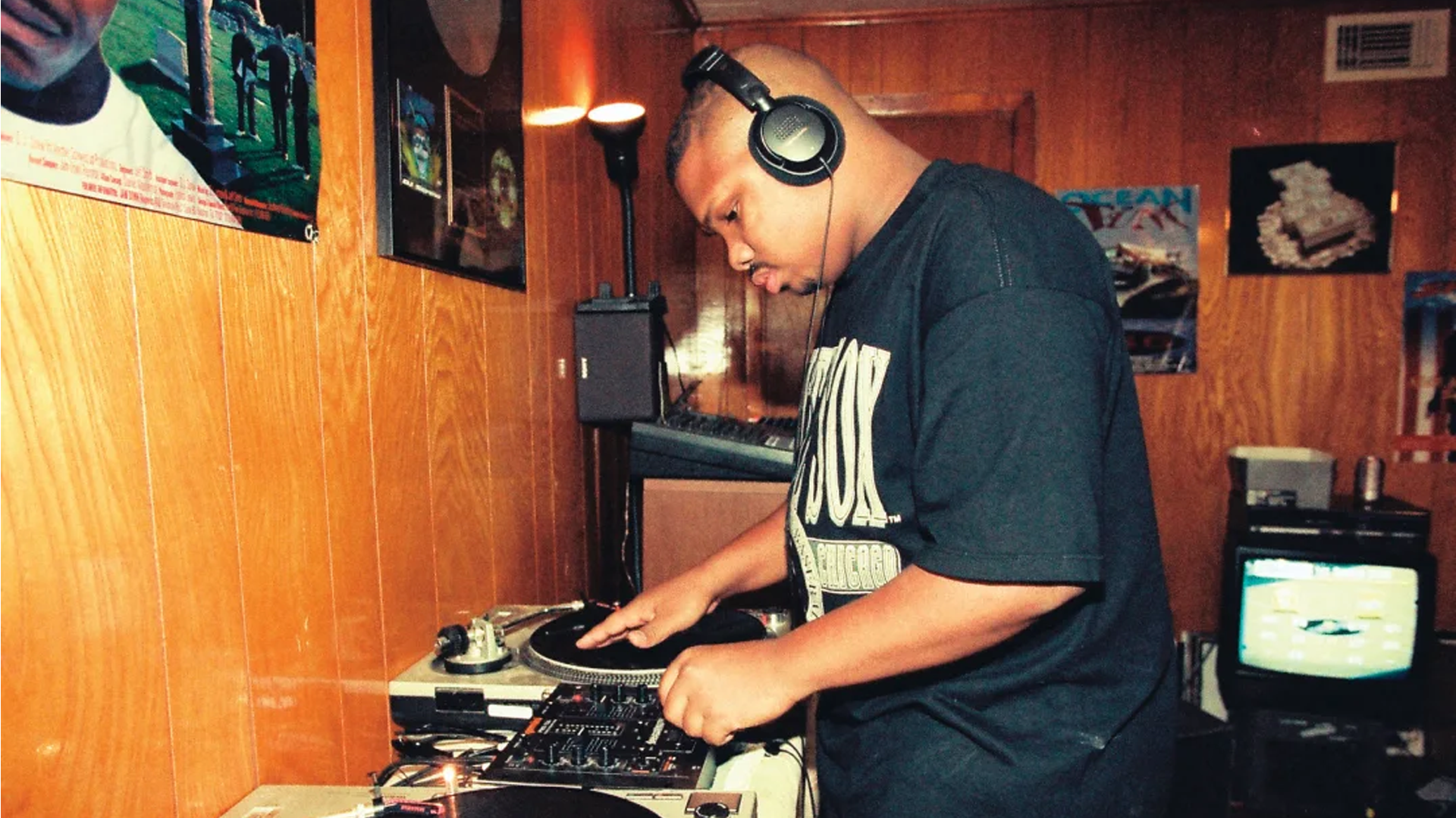 Man står vid en DJ-bord och mixar. Han har hörlurar på sig.