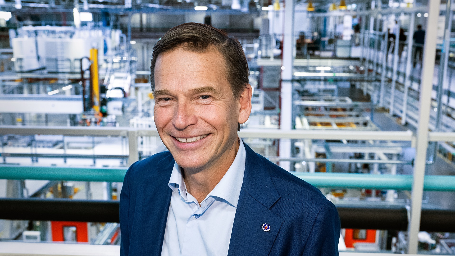 Porträtt av en man i mörkblå kavaj framför en industriell fabrik