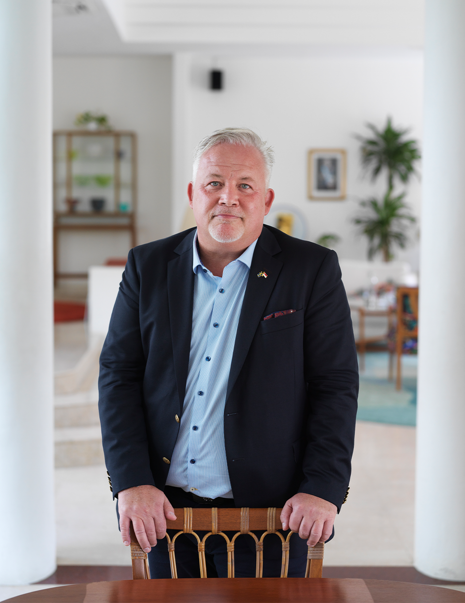 Kent Härstedt i sitt hem i Singapore. Han har händerna på en stol vid matbordet, och bär svart kostym.