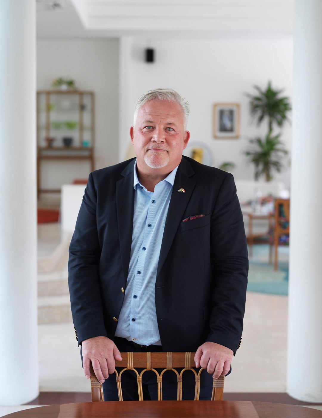 Kent Härstedt i sitt hem i Singapore. Han har händerna på en stol vid matbordet, och bär svart kostym.