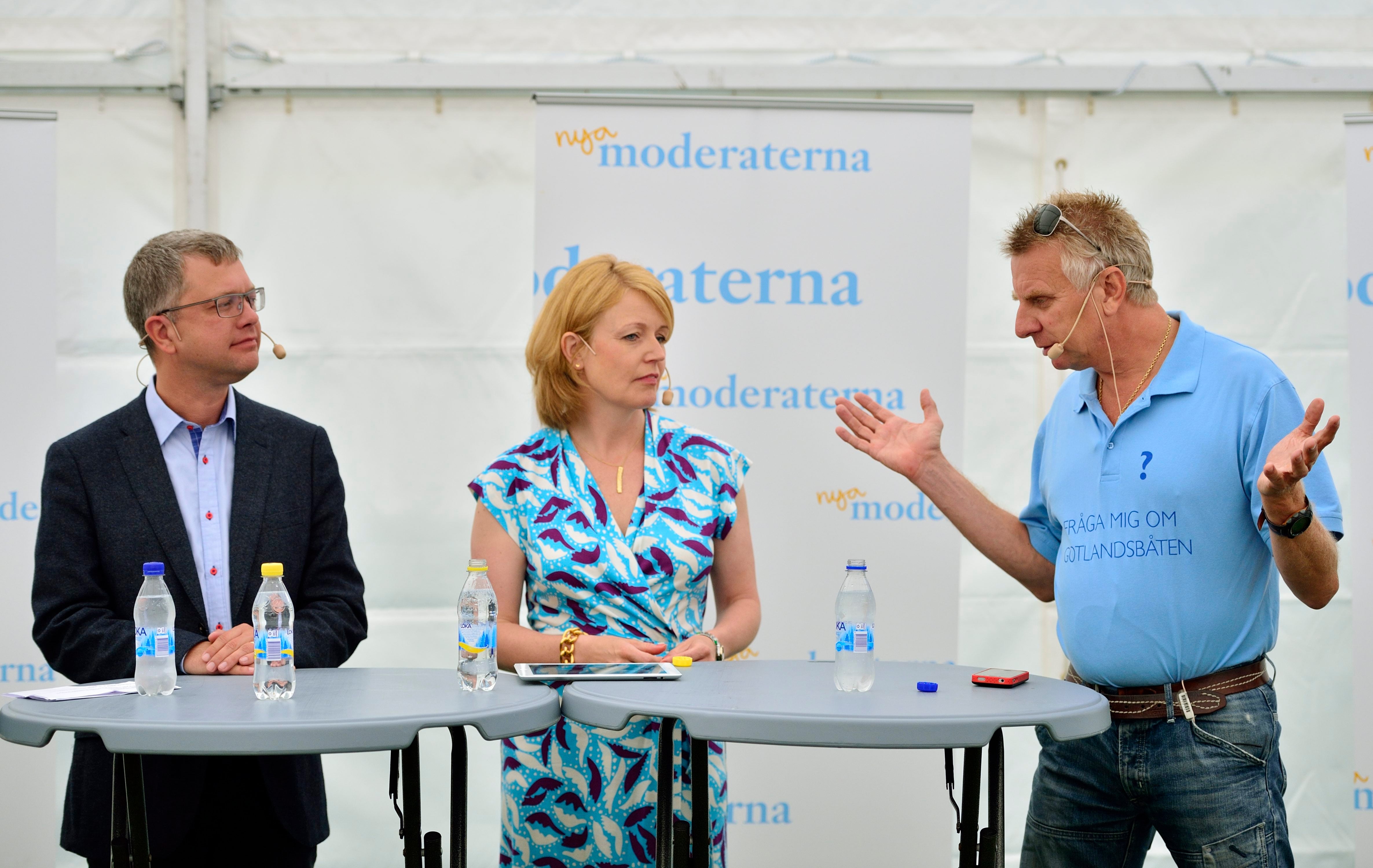 Tre personer sitter vid ett bord under en paneldiskussion på en konferens.