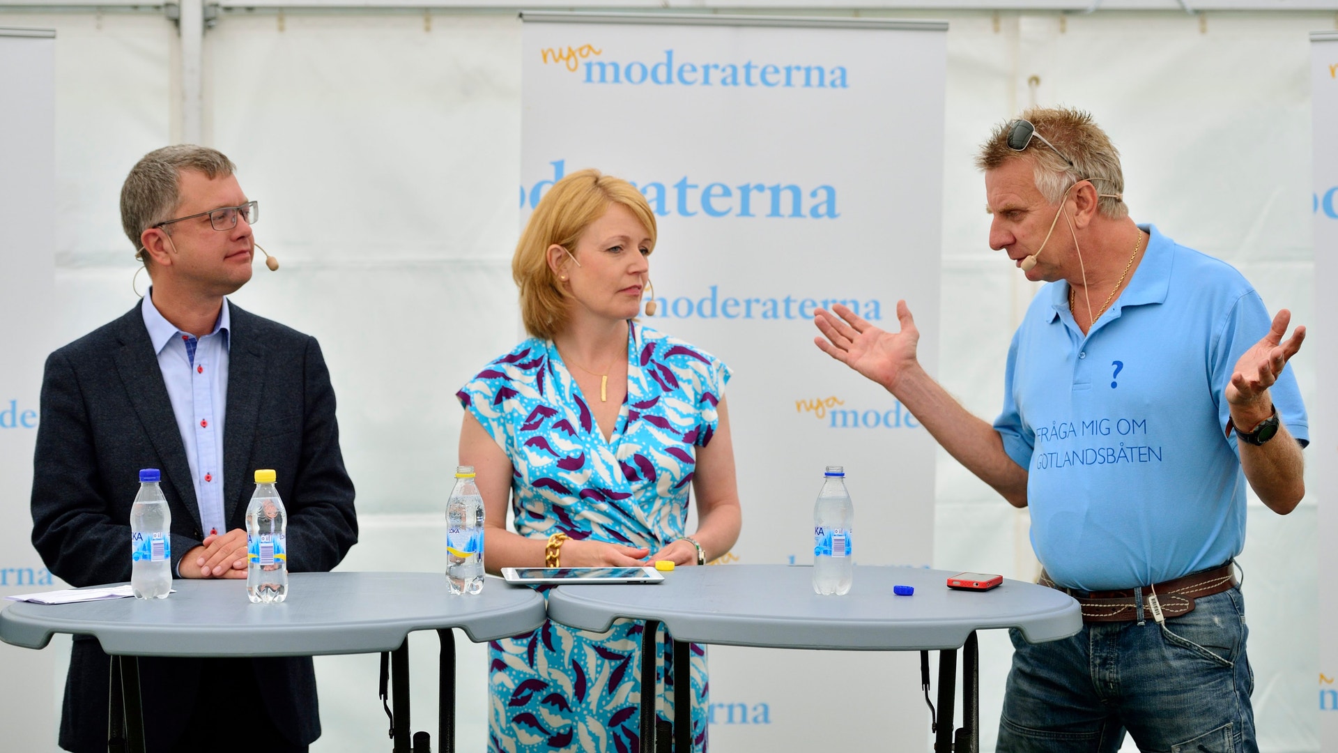 Tre personer sitter vid ett bord under en paneldiskussion på en konferens.