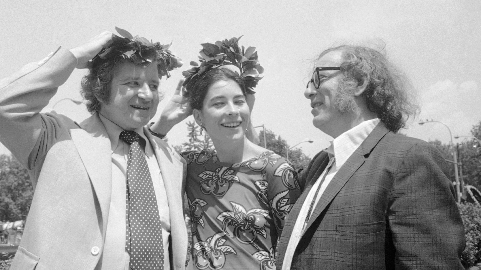 Svartvit fotografi av tre personer som står tillsammans utomhus och samtalar.