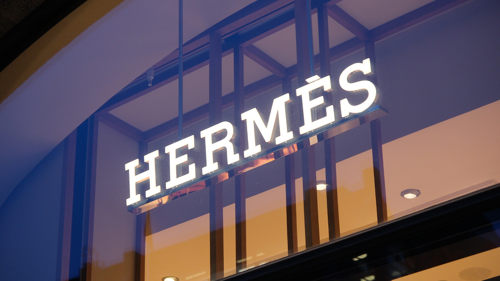 Upplyst skylt med texten Hermès ovanför en butiksingång.