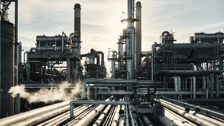 Industriell raffinaderi med rör, torn och ångutslipp mot molnig himmel.