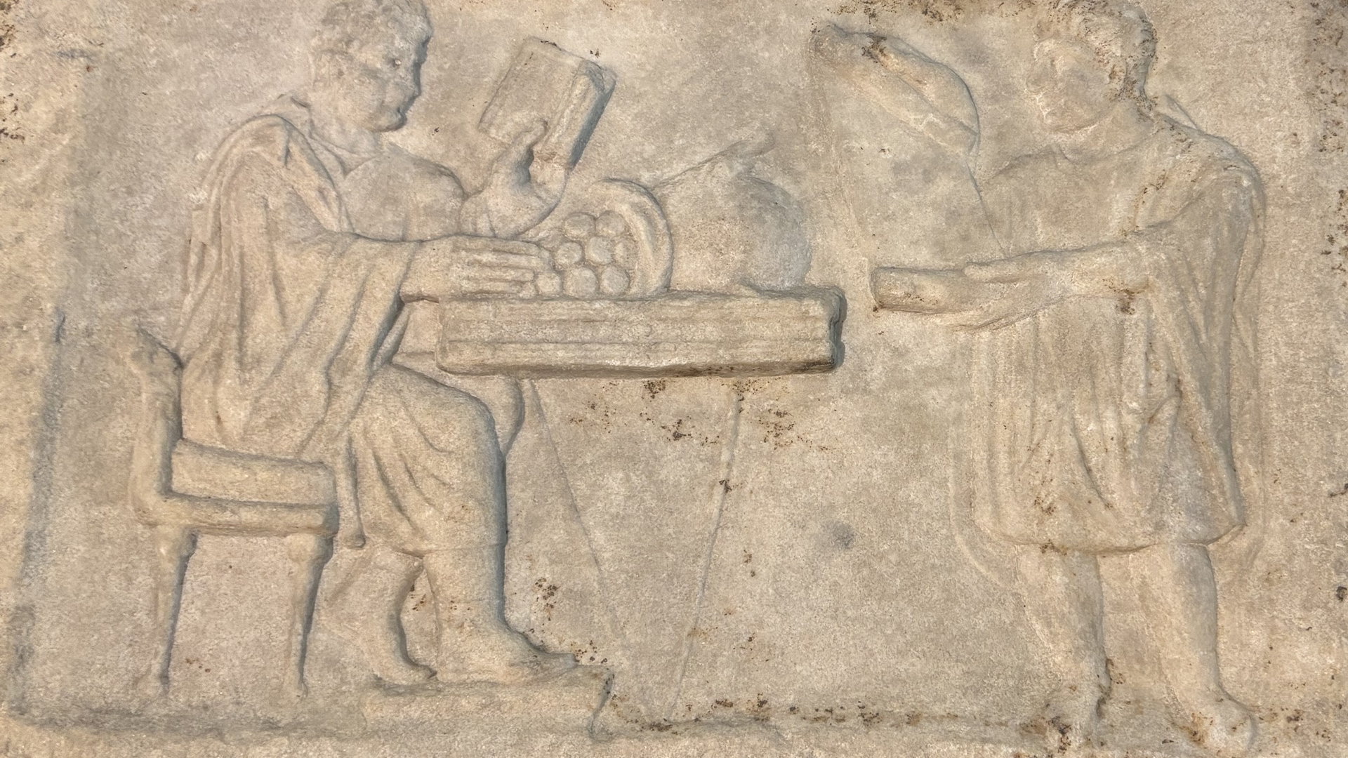Stenrelief som visar två figurer i antik stil som överför ett föremål mellan sig.