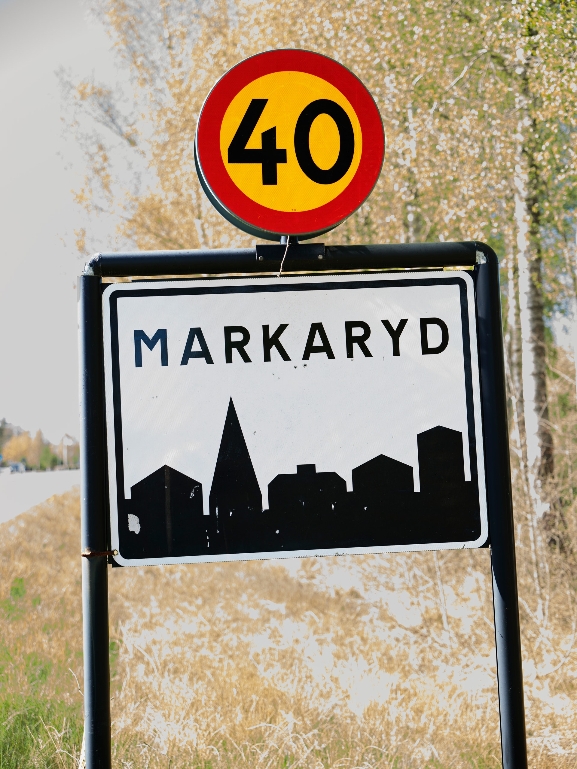 Vägskylt för Markaryd med hastighetsbegränsning 40 km/h. Skyltarna är monterade på en stolpe framför en vägg täckt av mossa och lav.
