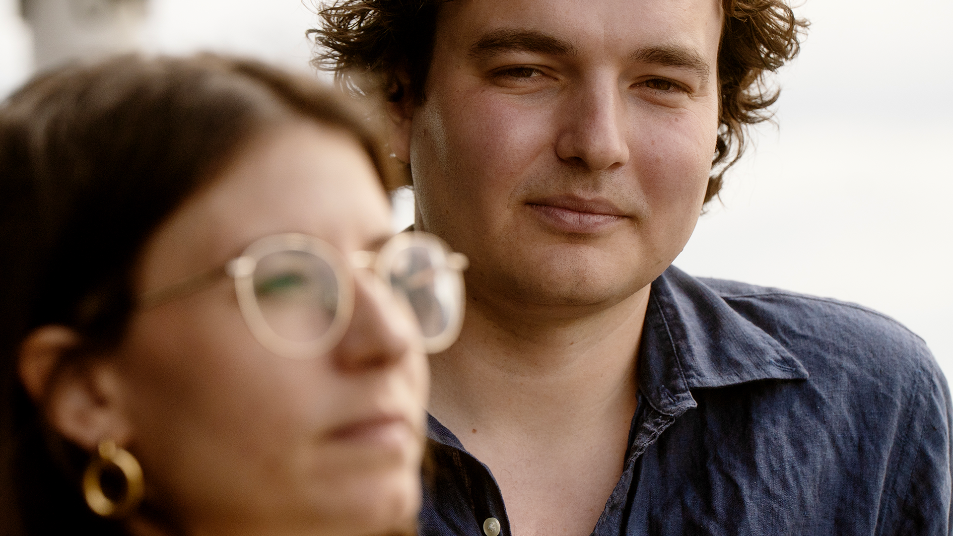 Hanna Andreen och Antonio Melani står på balkongen vid sitt kontor. Kameran har fokus på Antonio som tittar in i linsen.