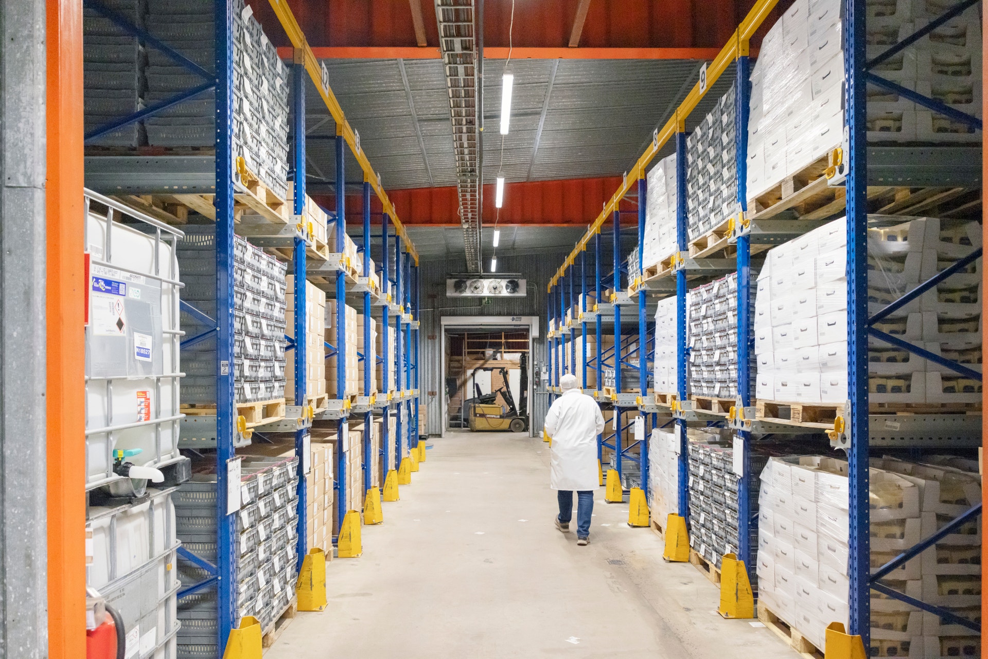 Lagerhall med höga hyllor fyllda med vita lådor. En arbetare i vit skyddsklädsel går genom mittgången. En gaffeltruck syns i bakgrunden.
