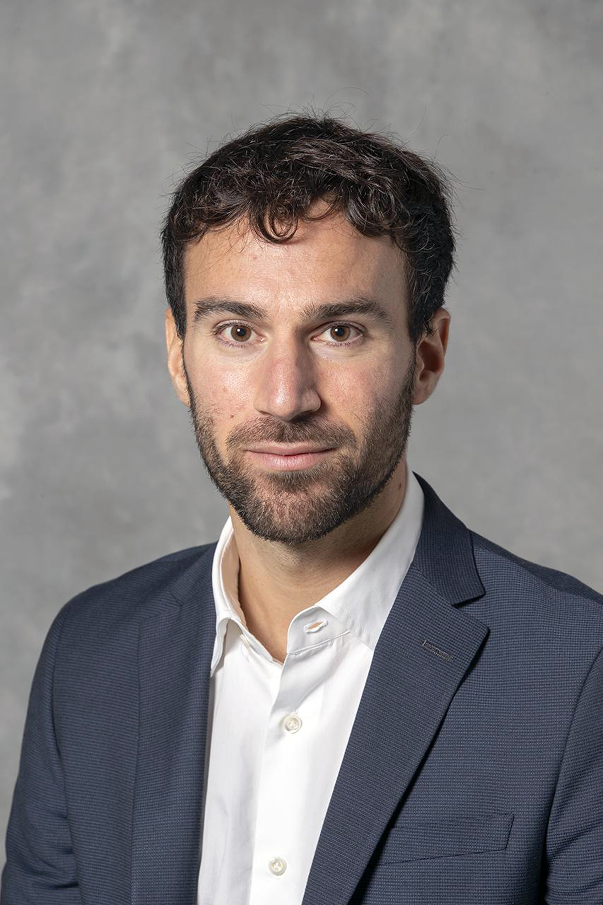 Porträtt av en man i professionell kläder mot neutral bakgrund.