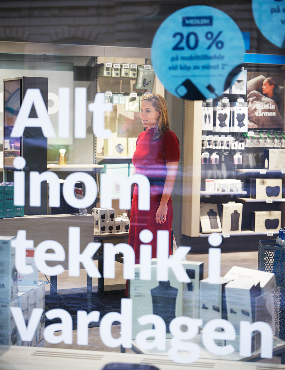 En kvinna står i en butik framför en skyltfönster med produktdisplayer och en blå rabattskylt.