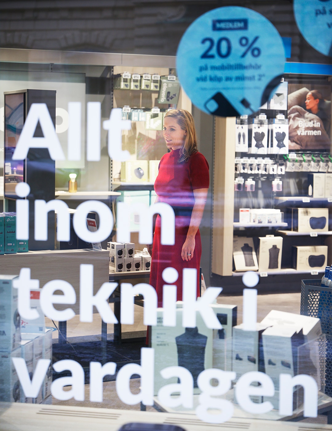 En kvinna står i en butik framför en skyltfönster med produktdisplayer och en blå rabattskylt.