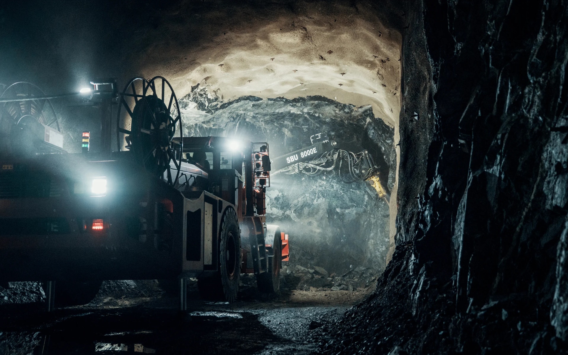 Gruvmaskiner med tända strålkastare i en mörk underjordisk gruvtunnel.
