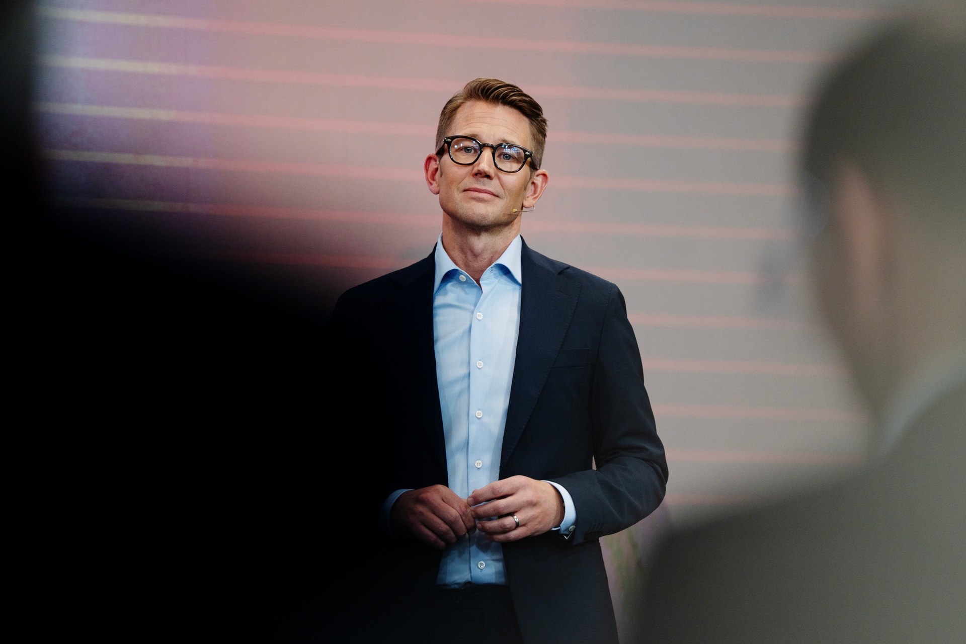 Man i glasögon och mörkblå blazer framför rosa bakgrund