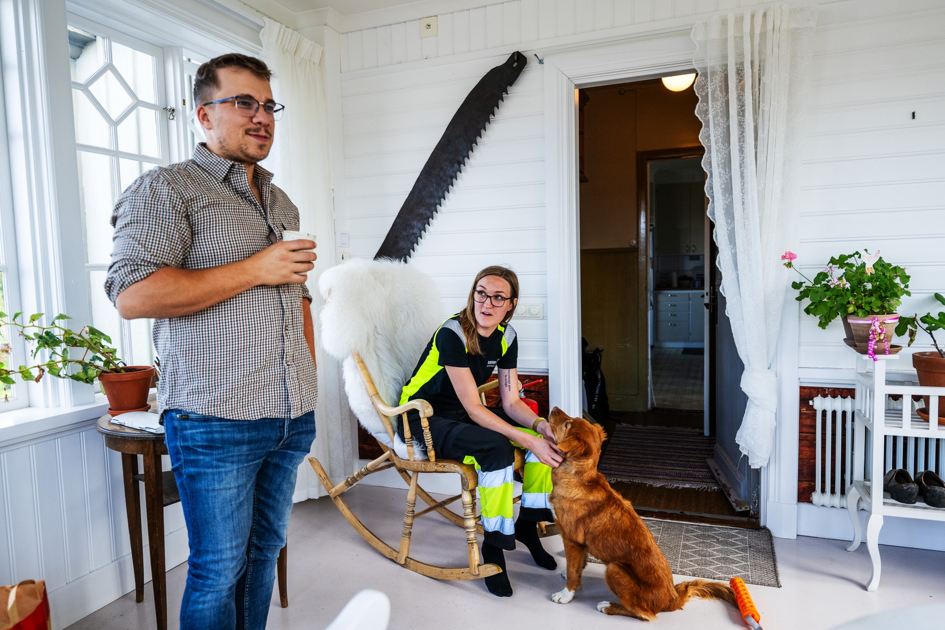 En man och en kvinna samtalar på en veranda medan en hund kliar sig mot kvinnans ben.