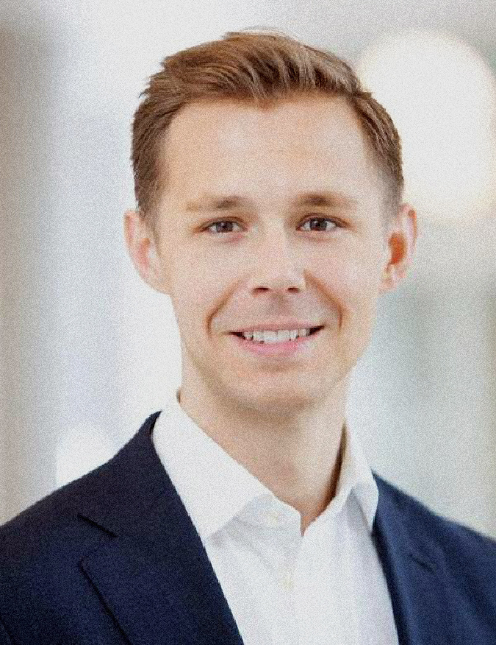 Porträtt av en man i mörkblå kavaj och vit skjorta som ler mot kameran mot en suddig bakgrund.