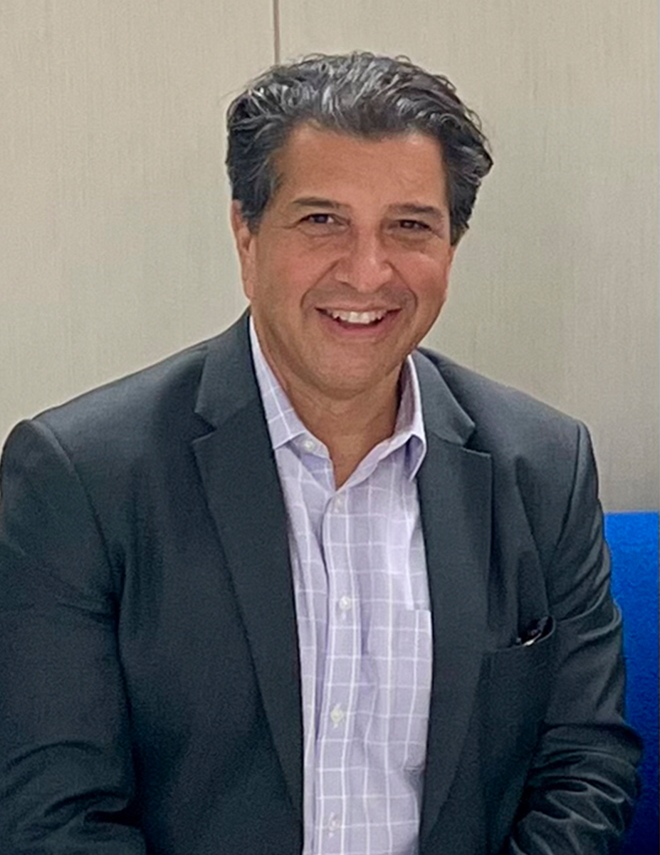 Gil Cisneros ler in i kameran på handelsbanken kontor i new york. Han har rutig blå skjorta och mörkgrå kavaj.