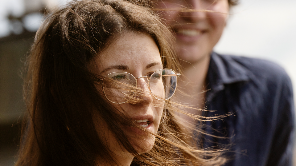 Hanna Andreen och Antonio Melani står på balkongen vid sitt kontor. Hannas hår flyger i vinden.