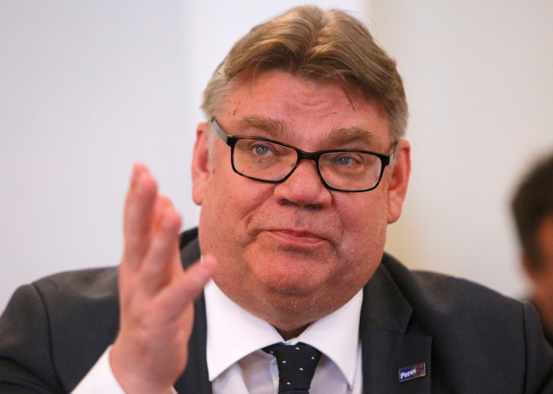 Man i kostym och glasögon gestikulerar med handen under ett möte.