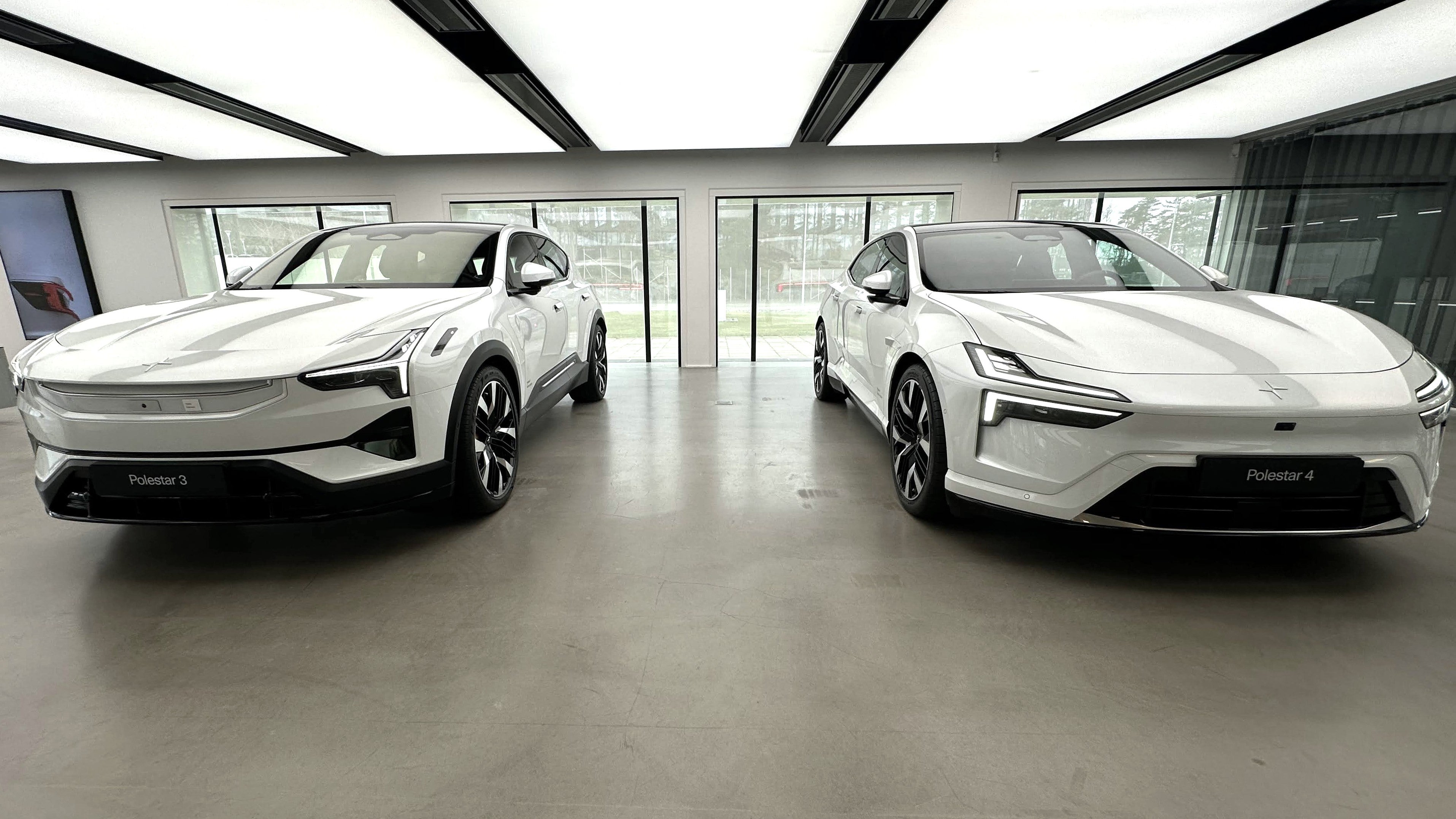 Två vita Polestar elbilar i ett modernt bilshowroom med stora fönster och minimalistisk inredning.