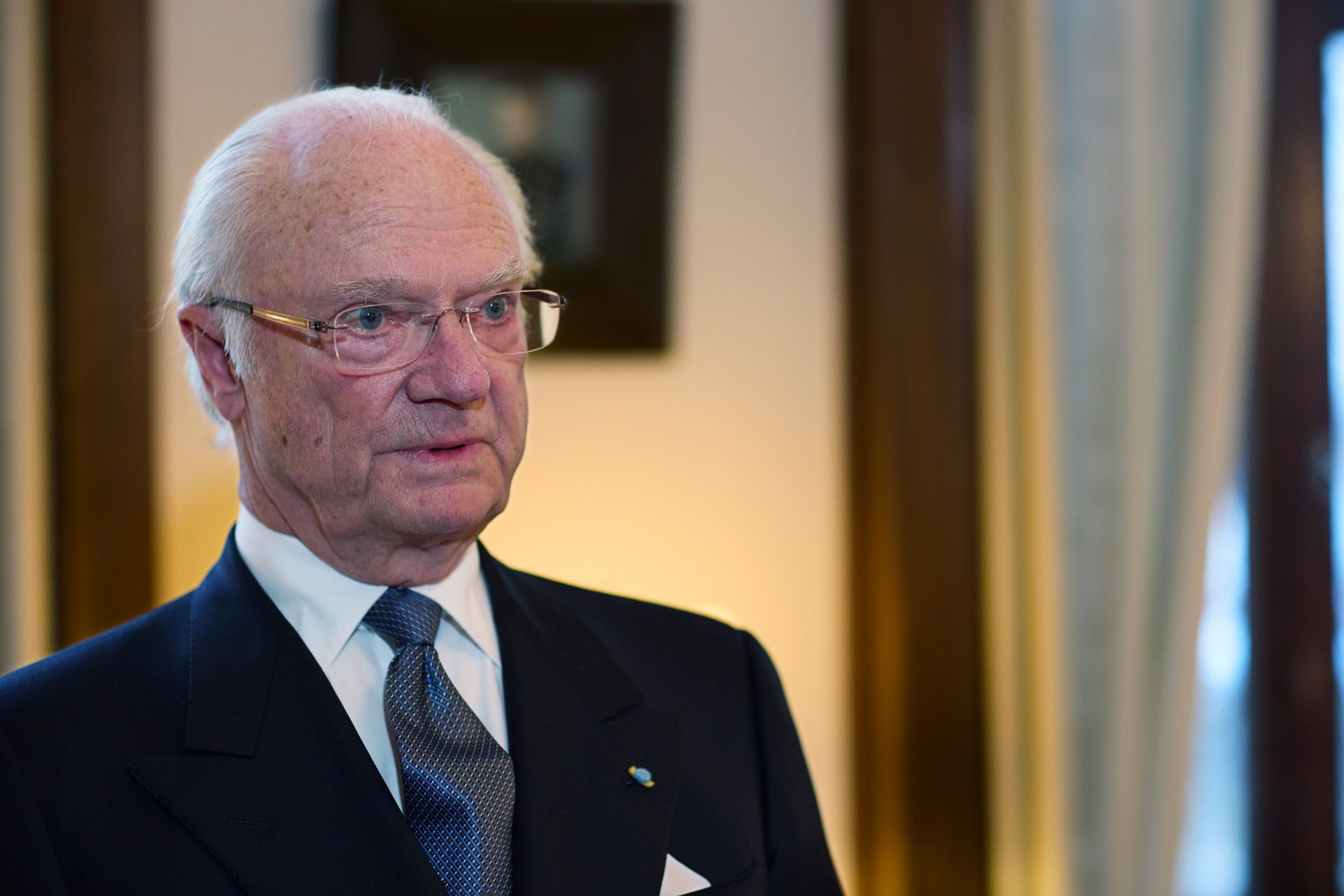 Porträtt av en äldre man i formell kostym och glasögon.