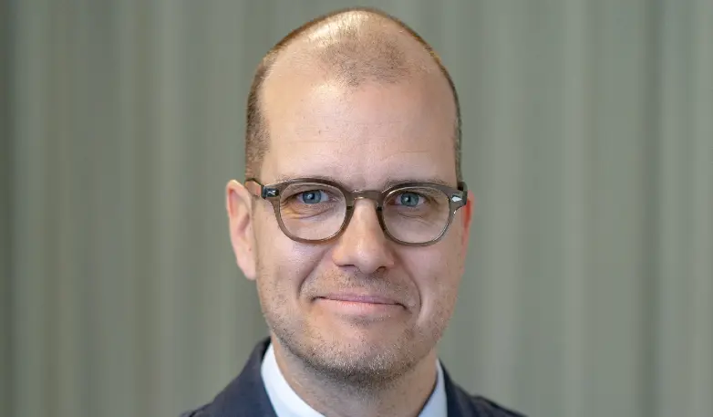 Joakim Bornold på en pressbild tagen av Söderberg och Partners. Han har bruna glasögon och ler in i kameran. 