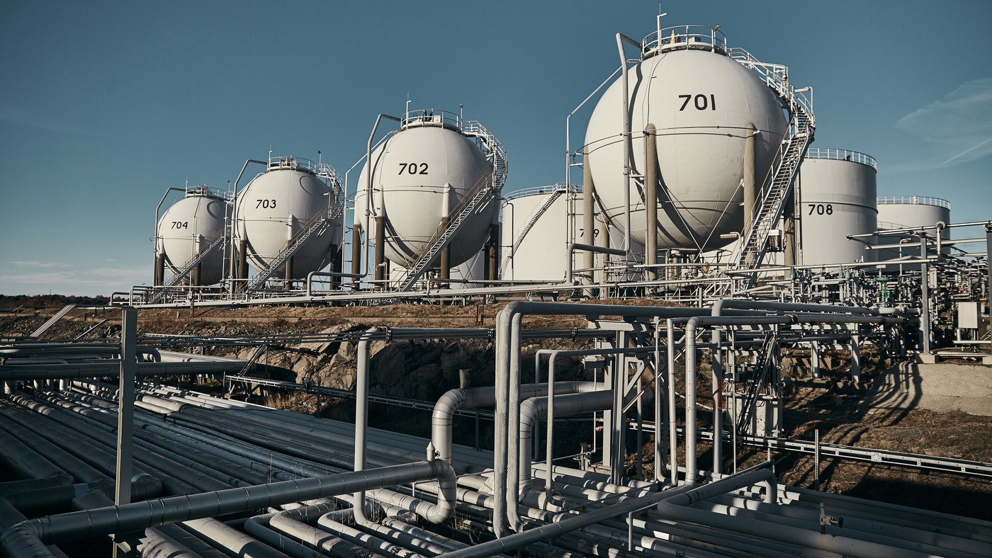 Industriell raffinaderi med flera vita lagertankar och rörsystem under klar blå himmel.