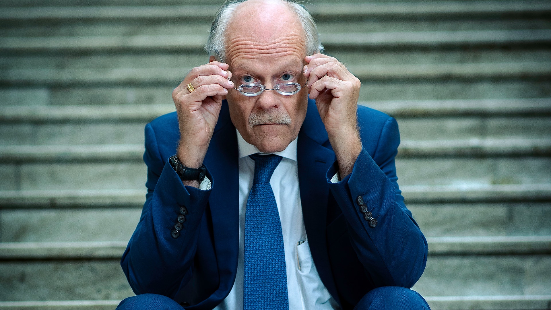 Stefan Ingves tittar fram över sina glasögon. Han sitter på en trappa.