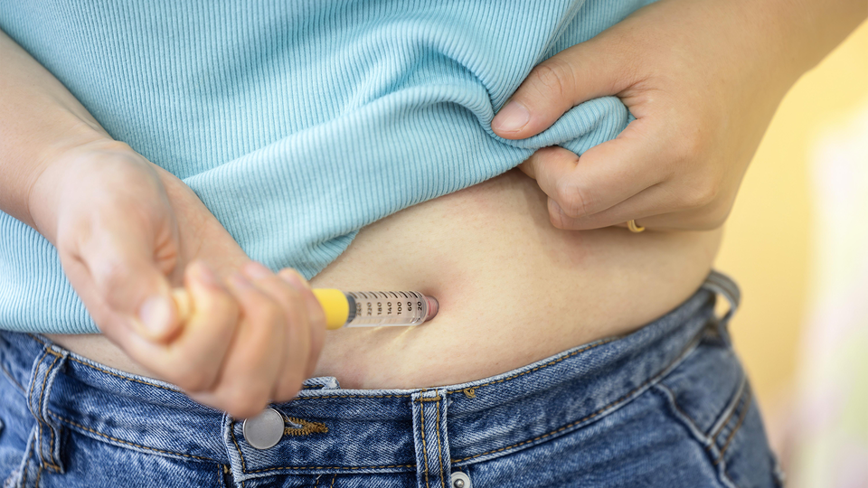 Person som håller en insulinpenna mot buken för att injicera insulin
