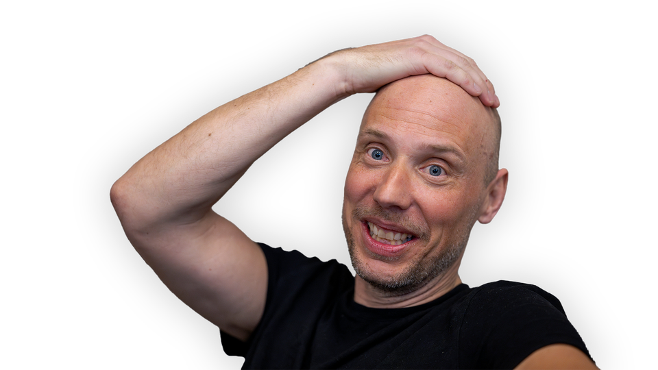 John Skogman ser glad ut. Han tar sig på huvudet. Han har svart t-shirt.