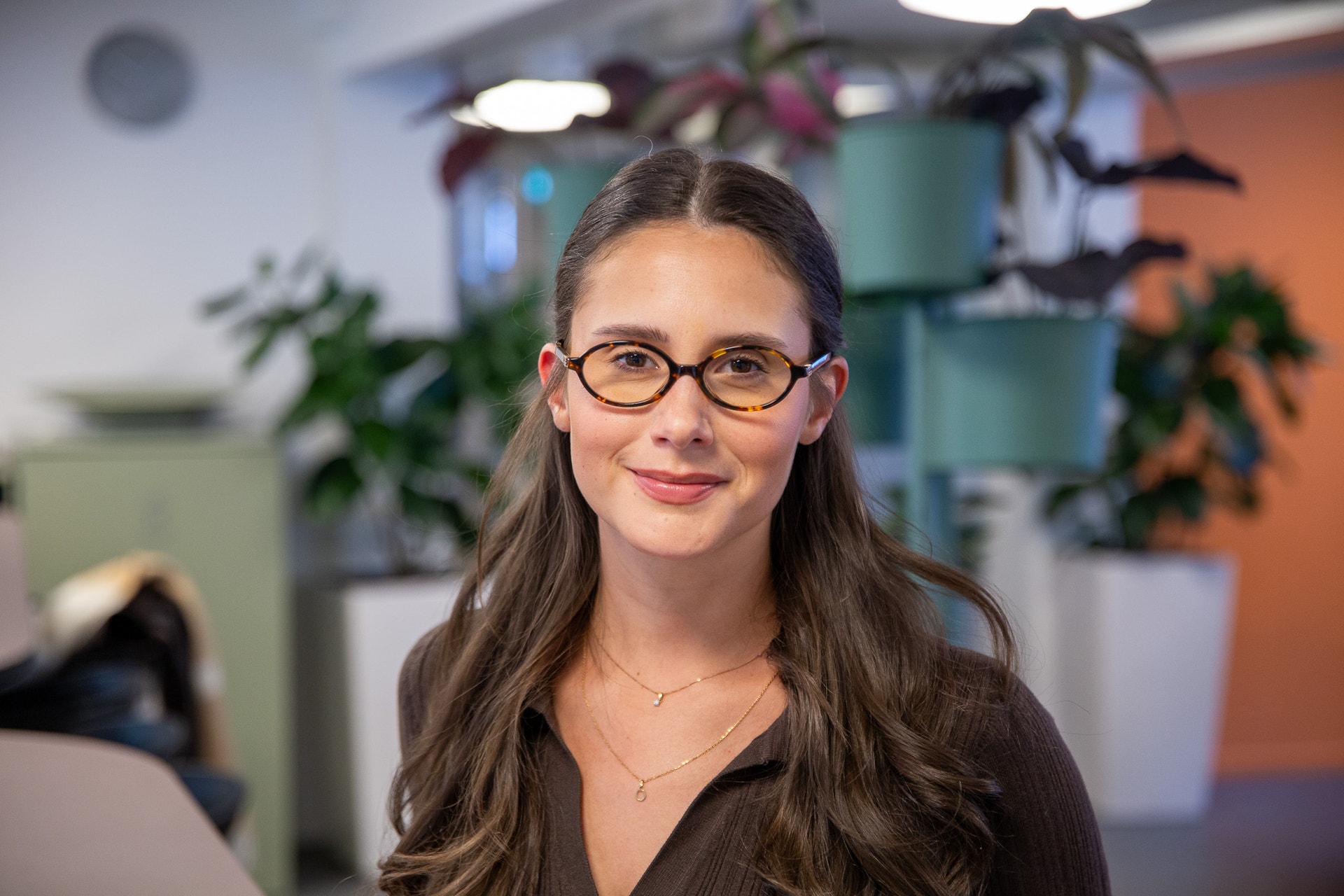 Porträtt av en kvinna med glasögon i ett modernt kontorsmiljö med växter i bakgrunden