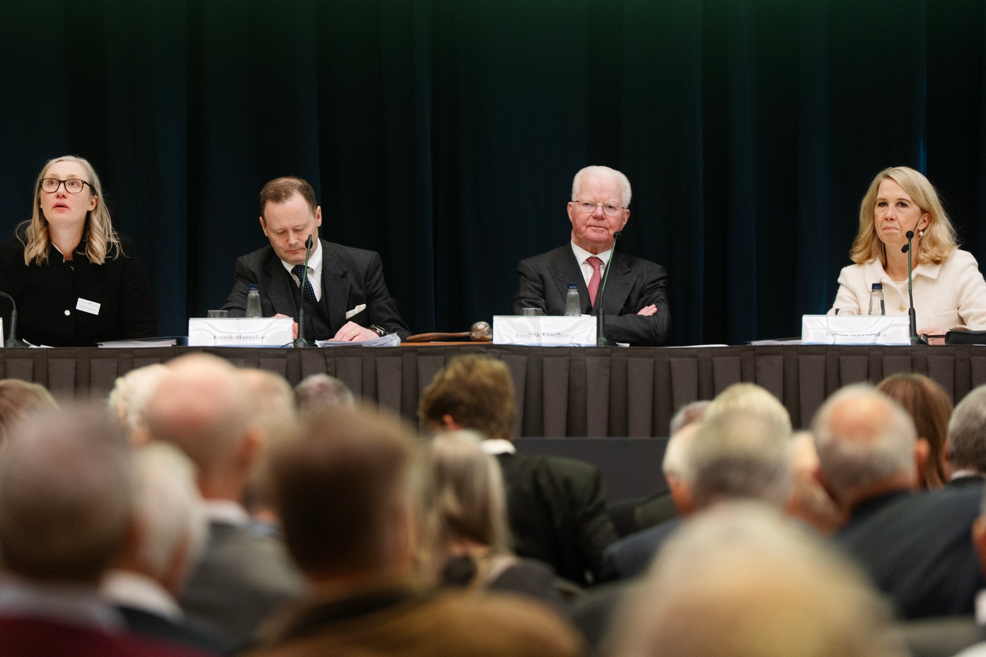 Fyra personer sitter vid ett bord under en konferens eller paneldiskussion framför en publik.